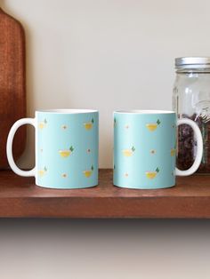 two coffee mugs sitting on top of a wooden shelf next to a glass jar