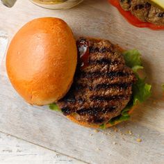 a hamburger sitting on top of a wooden cutting board next to a bowl of pickles