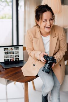 a woman sitting at a table with a camera in her hand and smiling for the camera