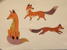 three embroidered pictures of foxes on white fabric