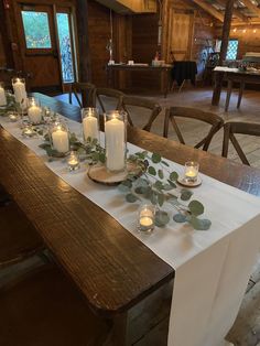 a long table with candles and greenery on it in a large room filled with wooden chairs