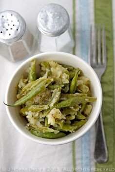 a white bowl filled with green beans and mashed potatoes next to a fork on a table