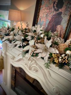 a mantel decorated with white flowers and greenery on top of a mantle in front of a painting