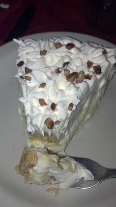 a white plate topped with a piece of cake covered in whipped cream and pecans