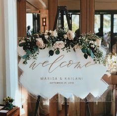 a welcome sign with flowers and greenery on it