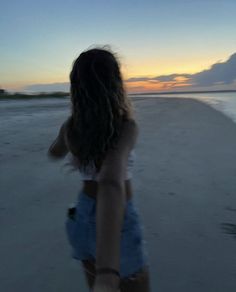 a girl walking on the beach at sunset with her back to the camera and arms behind her