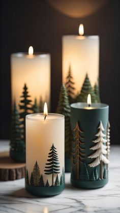 three lit candles sitting on top of a table next to each other with trees painted on them