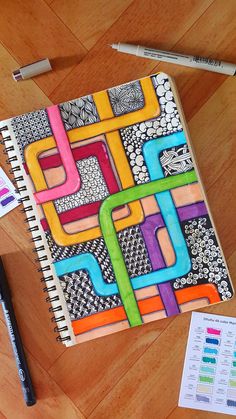 a notebook covered in colored paper next to markers and pencils on a wooden floor