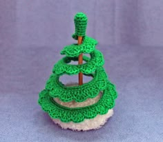 a crocheted green christmas tree sitting on top of a white cupcake covered in frosting