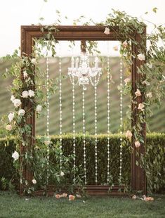 a wooden frame with white flowers and pearls hanging from it is surrounded by greenery