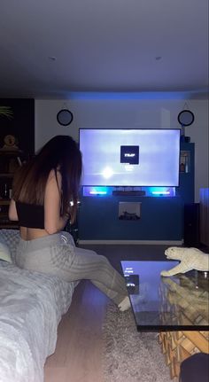 a woman is sitting on the floor in front of a large screen tv and watching television