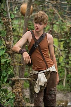 a young man standing next to a tree in the woods wearing a harness and climbing gear