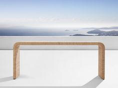 a wooden table sitting on top of a white floor next to an ocean and sky