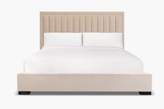 a bed with white sheets and beige headboard