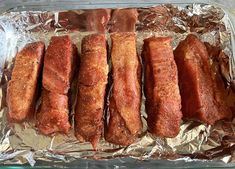 four pieces of meat on tin foil lined up in a baking pan, ready to be cooked