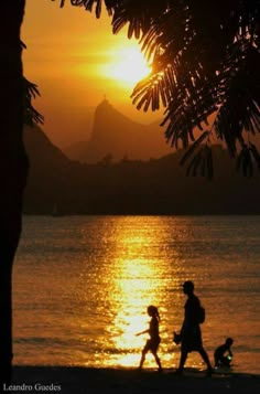 people walking on the beach at sunset with mountains in the backgrouund and water behind them