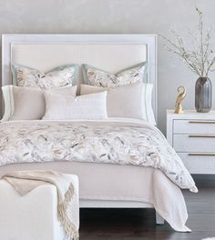 a white bed sitting in a bedroom next to a night stand and dresser with flowers on it