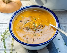 a blue and white bowl filled with soup on top of a wooden table next to a pumpkin