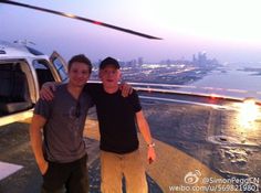 two men standing next to each other in front of a helicopter