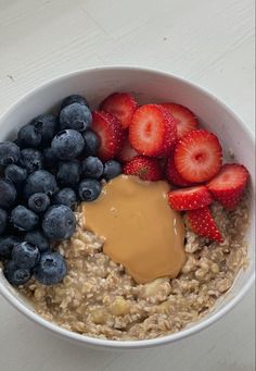 a bowl of oatmeal with strawberries and blueberries on the side