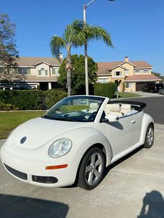 a white convertible car parked in front of a house with palm trees and houses behind it