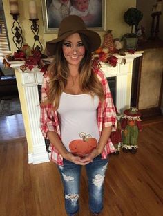 a pregnant woman standing in front of a fireplace holding an apple and smiling at the camera