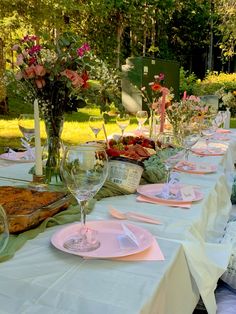 a long table is set up with pink plates and place settings for an outdoor party