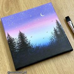 a painting on a wooden table with a pen and paper in front of it that has trees painted on it