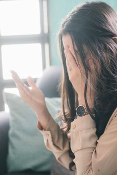 a woman sitting on top of a couch holding her hand up to her face