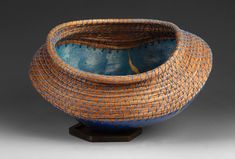 a blue and orange bowl sitting on top of a wooden stand in front of a gray background