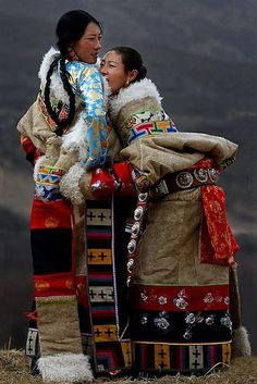 two women dressed in native clothing standing next to each other on top of a hill