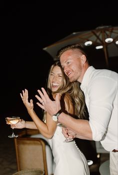 a man and woman standing next to each other holding hands in front of an umbrella