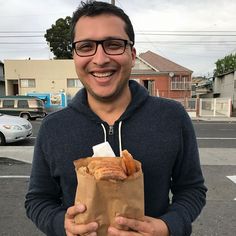 a man holding a bag full of food in front of his face and smiling at the camera