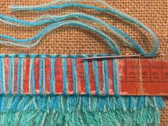 a piece of blue and red yarn sitting on top of a brown table next to a ruler