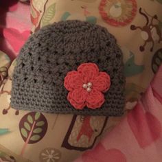 a crocheted hat with a flower on it sitting on a bed next to a pillow