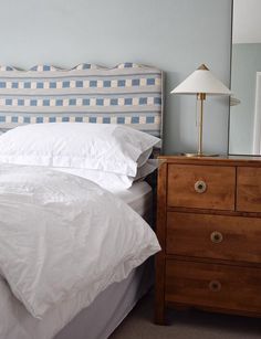 a bed with white sheets and blue checkered headboard next to a night stand