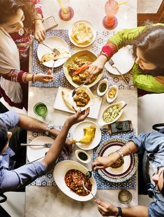 several people sitting at a table with plates and bowls of food in front of them