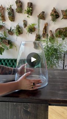 a woman sitting at a table with a glass vase filled with plants