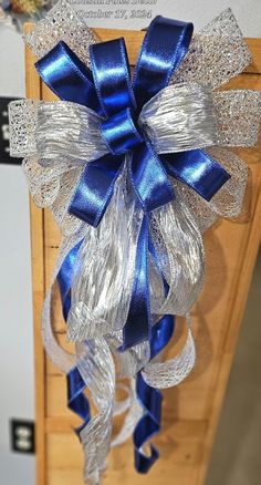 a large blue and silver bow hanging from the side of a wooden door with ribbon on it