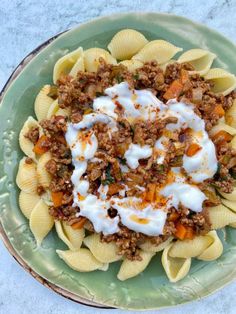 a green plate topped with pasta and meat covered in sauce on top of it's own