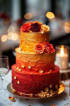 a multi - tiered cake with red and yellow frosting on a table next to candles