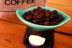 coffee beans in a green bowl on a wooden table next to a lit tea light