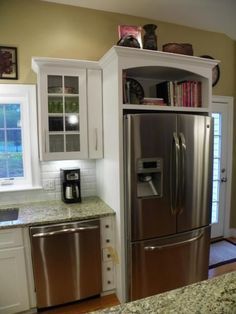 a stainless steel refrigerator in a kitchen next to a sink and window with white cabinets