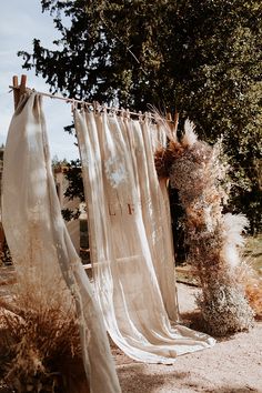 an old curtain is hanging on a clothes line outside in the sun with dry grass and trees behind it