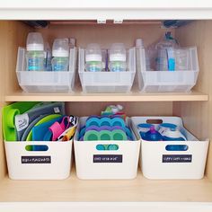 three plastic bins filled with baby items on top of a wooden shelf in a closet