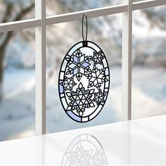 an egg shaped ornament hanging on a window sill in front of snow covered trees