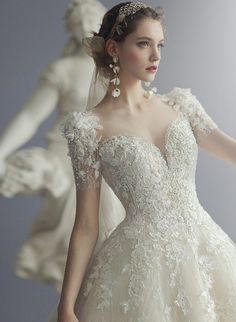 a woman in a wedding dress is holding her hand out to the side, with statues behind her