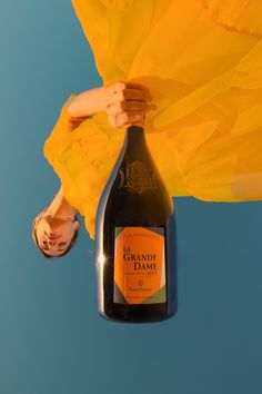 a bottle of orange wine is held up by a woman's legs and yellow umbrella