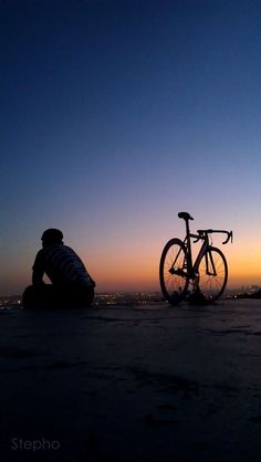 a person laying on the ground next to a bike at sunset with city lights in the background