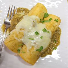 a white plate topped with food covered in sauce and cheese next to a silver fork